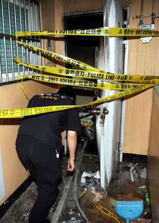 A police officer ducks under crime scene tape restricting access to the burnt out apartment in Ulsan in September 2006